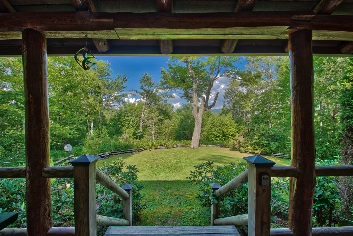 A charming wooden porch overlooking an expansive lawn framed by tall trees and lush plantings. The inviting setup encourages relaxing with friends after a day of mountain adventures, enjoying peace and camaraderie outdoors.