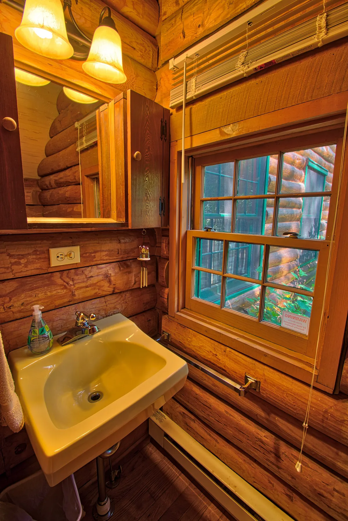 A warm and inviting bathroom scene with a sink, window, mirror, and wooden cabinets. Natural light streams in through the window, offering a quiet moment of relaxation and a glimpse of the natural surroundings.