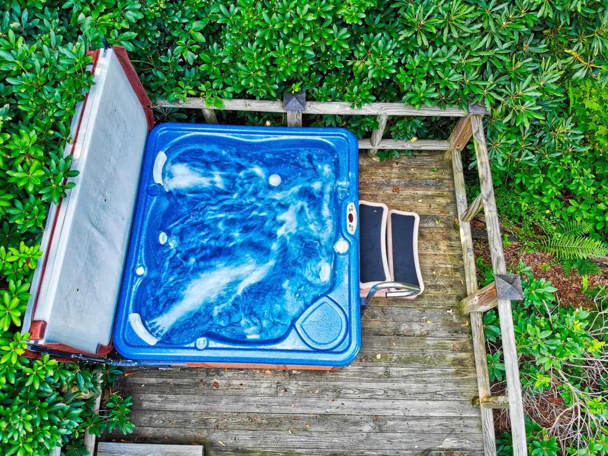 A tranquil outdoor hot tub and lounge chair are surrounded by lush greenery. The serene setting is ideal for relaxing after a day of adventure, stargazing with family, or sharing quiet moments in nature. The scene captures both comfort and immersion in the outdoors.