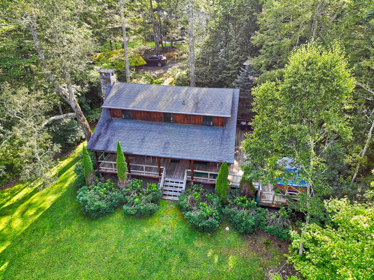 A picturesque exterior shot of the log cabin nestled among lush greenery, with a welcoming deck and garden area. The scene hints at peaceful outdoor gatherings, with space for friends to relax on the porch and enjoy the surrounding nature.