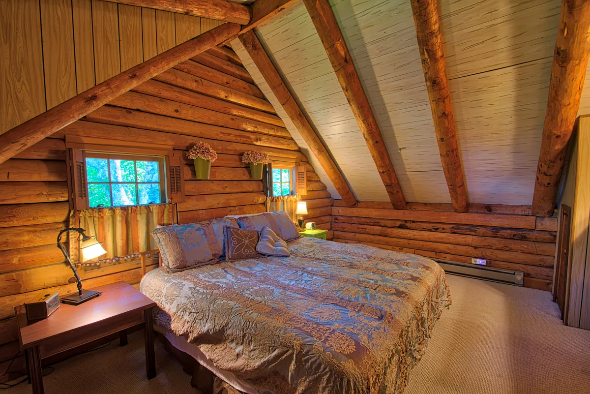 This interior shot focuses on a bedroom or sitting area with exposed wooden beams, a bed with a decorative cover, windows adorned with floral arrangements, and a nightstand with a lamp. The natural light pouring in and comfortable atmosphere underscore the pet-friendly, homey qualities described in the section.