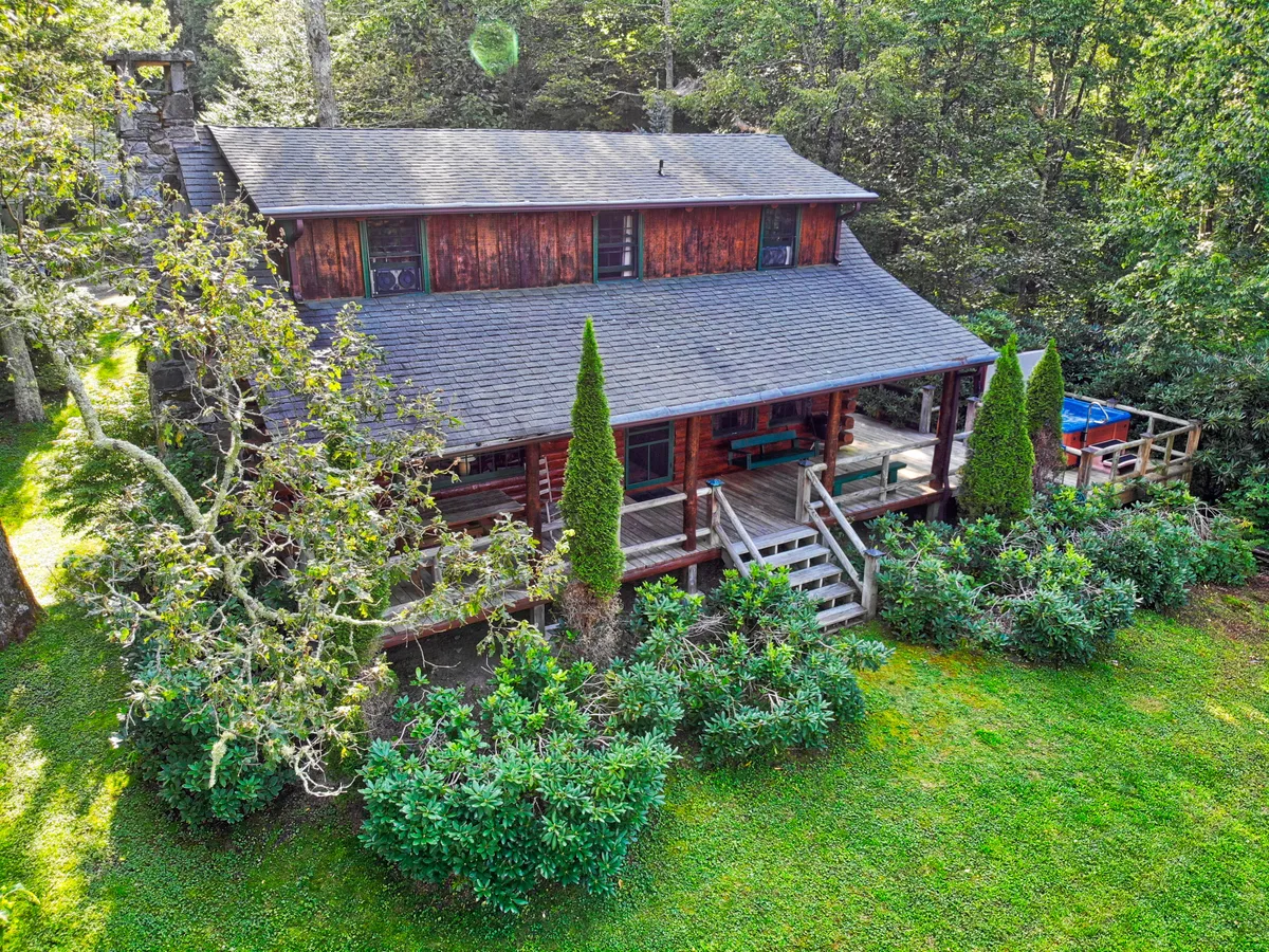A cozy log cabin is nestled amidst lush greenery. The welcoming deck features comfortable seating, perfect for family gatherings or enjoying meals outdoors. The surrounding area invites exploration, with ample space for children to play, pets to roam, and adults to relax. The view suggests easy access to natural beauty and outdoor adventure.