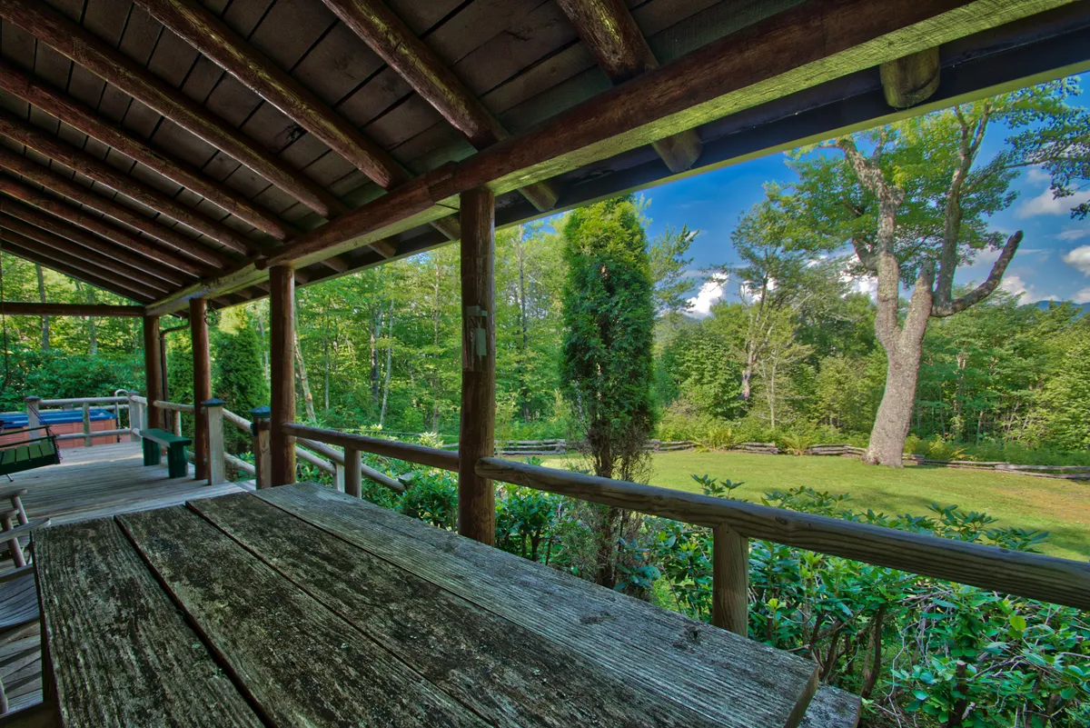 An exterior view of a wooden picnic table under the shelter of wooden beams, surrounded by lush greenery. The setting suggests opportunities for outdoor dining, morning coffee, or simply soaking in the peaceful ambiance of nature.